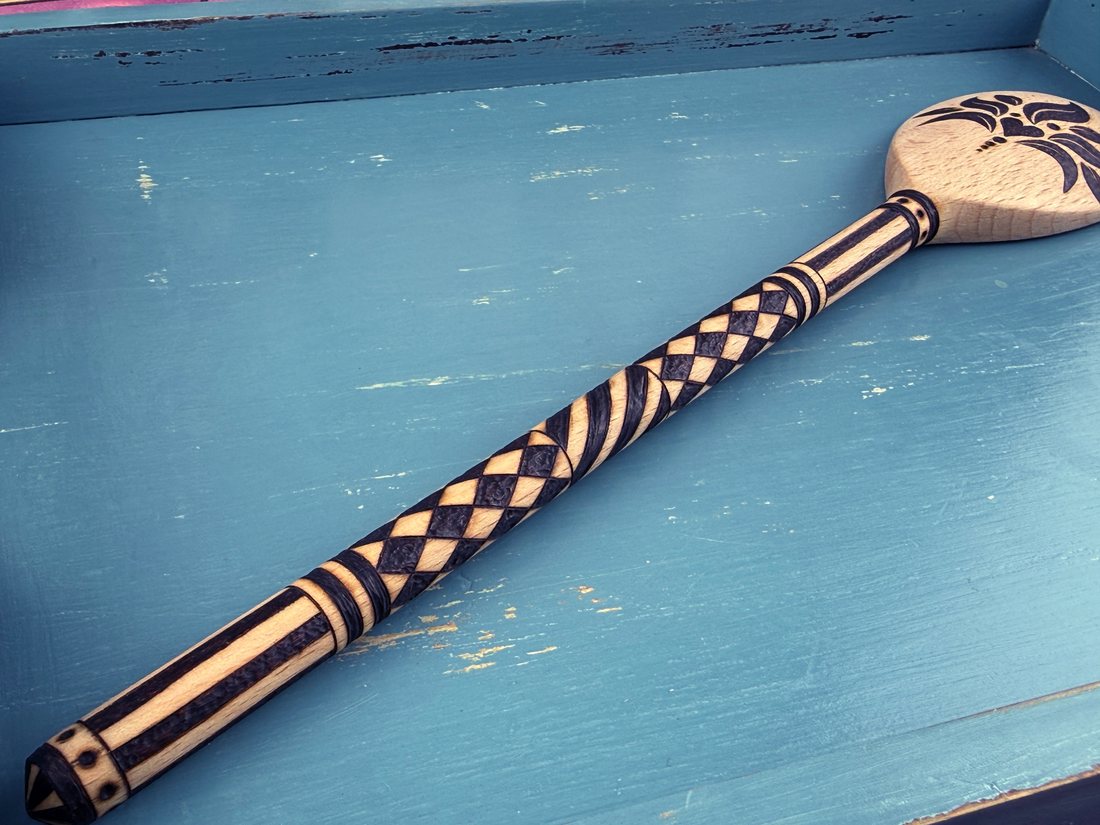 Close-up of a chequered pyrography spoon handle on a blue tray