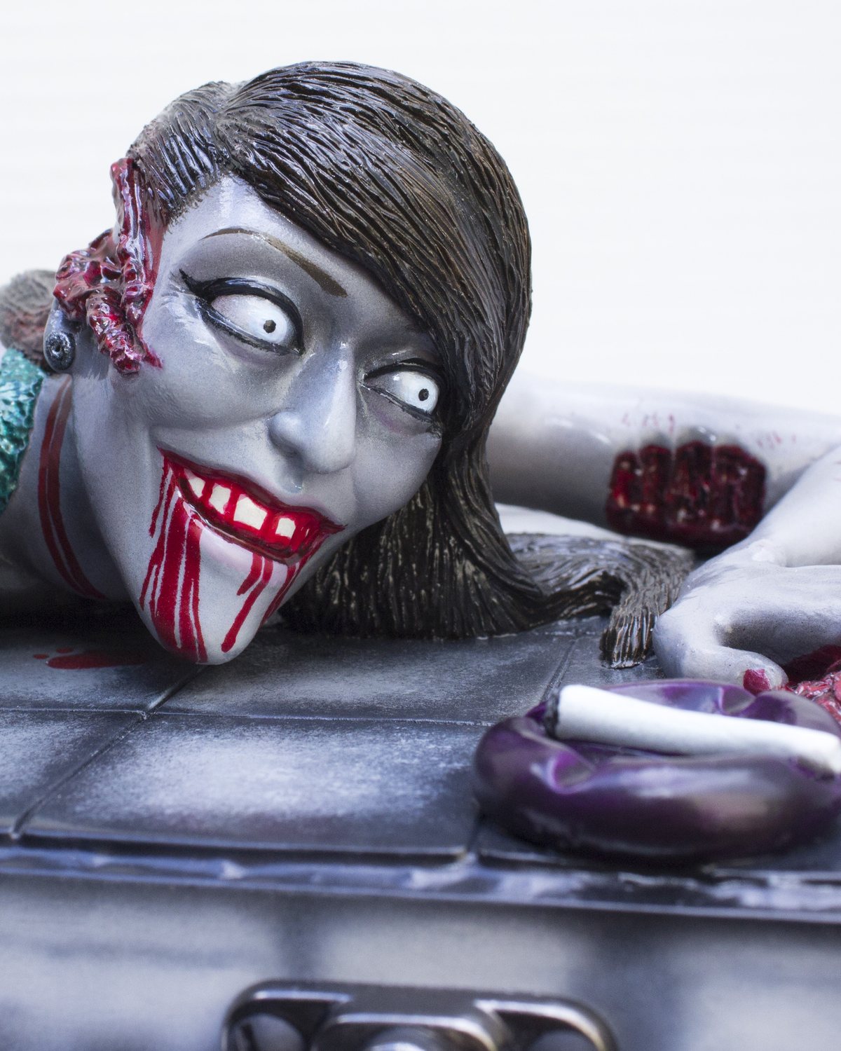 Sculpted zombie figure's face and torn ear, lying across a tiled chest with blood detailing